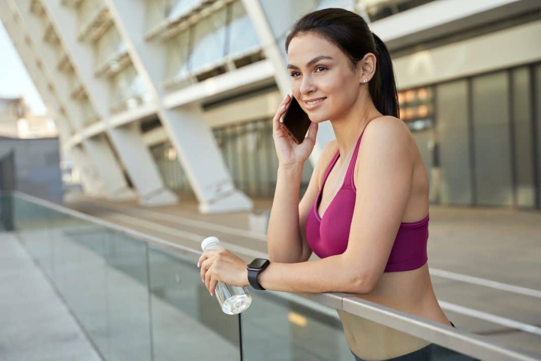 Smiling sportswoman with mobile phone and bottle of water at the stadium