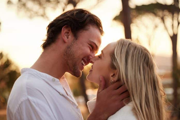 Love, happy and kiss with couple in nature for romance, bonding and affectionate together. Sensual,