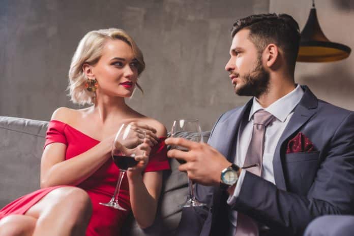seductive young couple holding glasses of wine and looking at each other