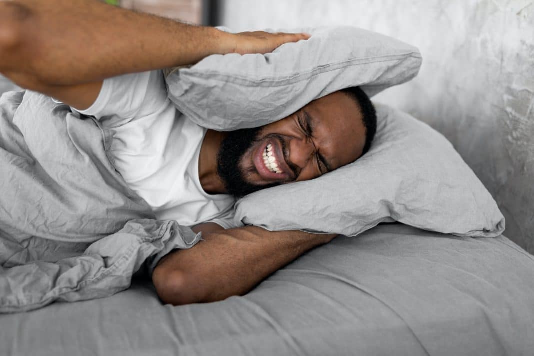 Stressed black man covering ears lying in bed