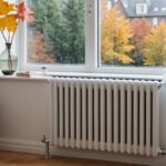 Hand stellt das Thermostatventil eines Heizkörpers unter einem Fenster ein