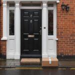 A cardboard parcel left outside the front door of a red-brick British terraced house on a wet, overcast day